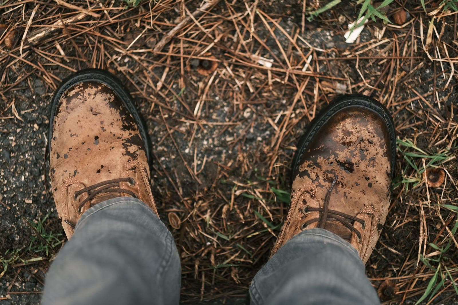 Rugged brown leather boots stained with dirt on an outdoor surface