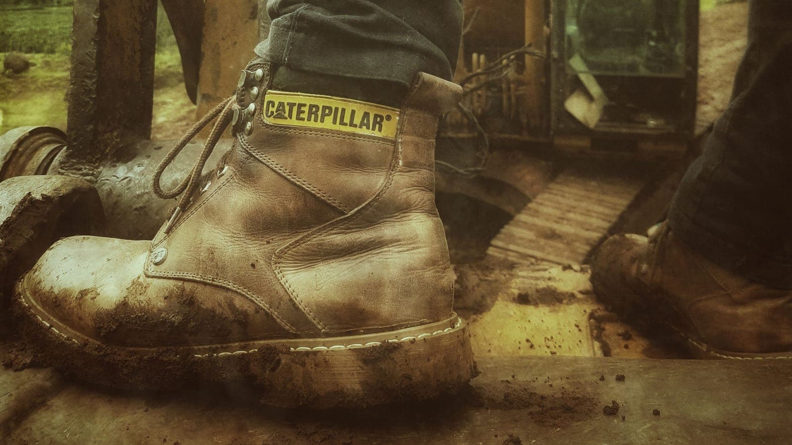A rugged work boot on a muddy construction site with soil packed into the tread