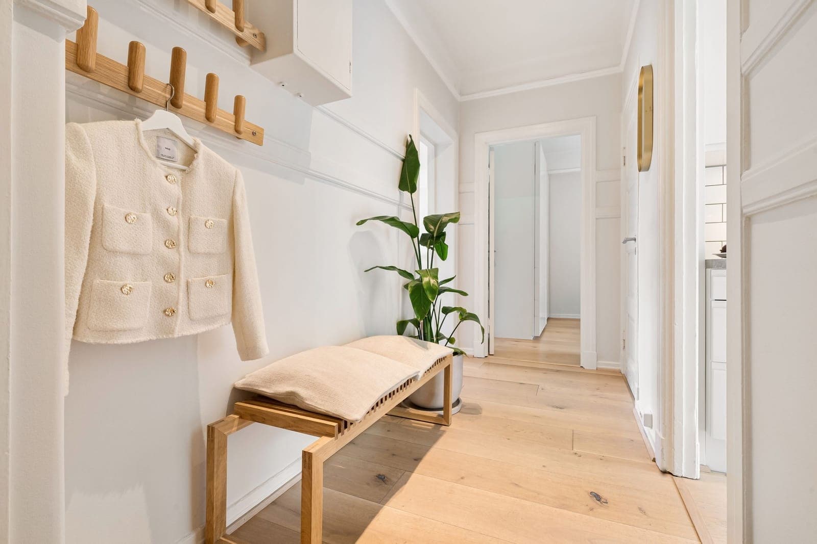 A bright hallway with a wooden bench and a coat hanging on the wall above it