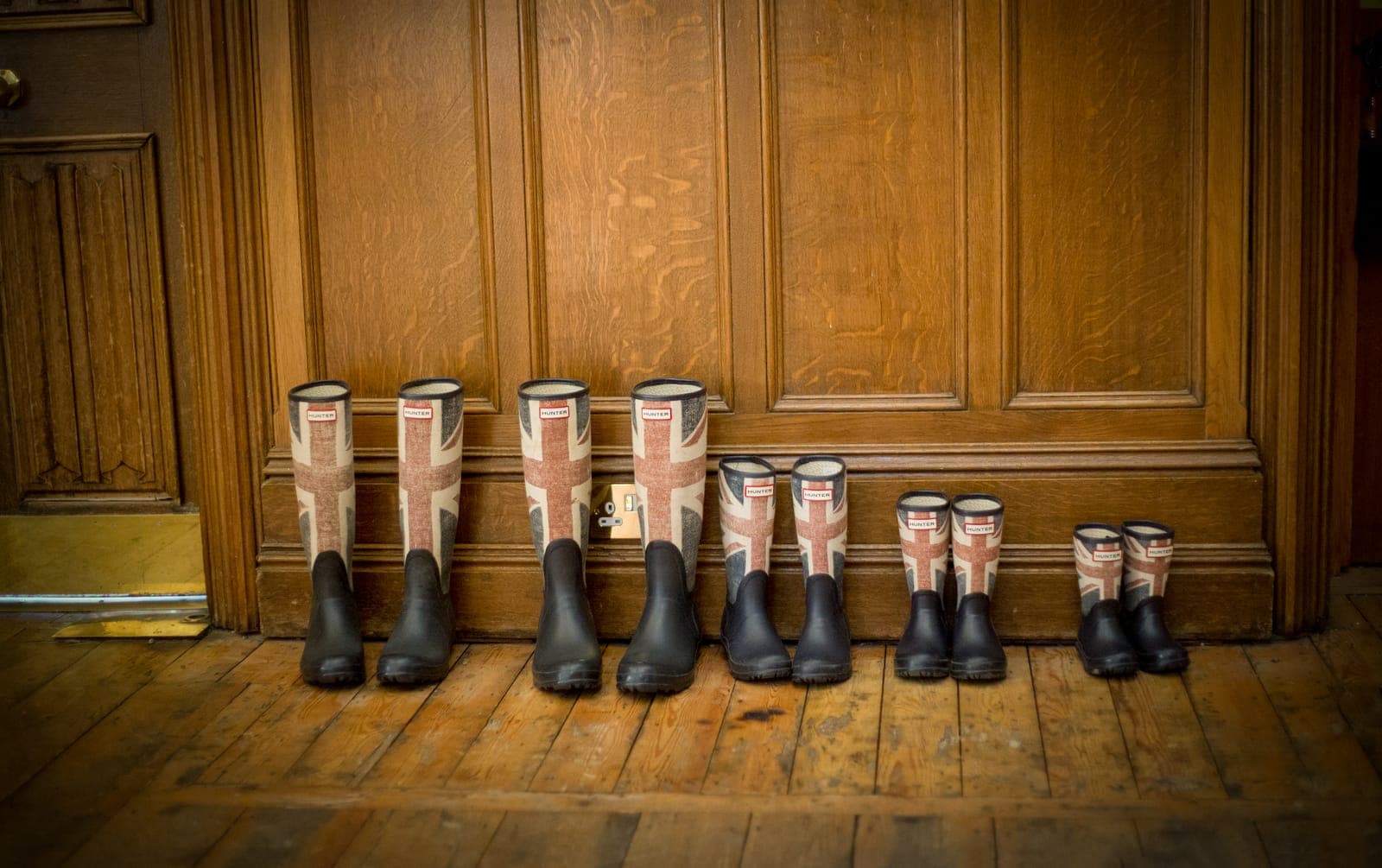 Four pairs of rain boots lined up neatly on a wooden floor indoors