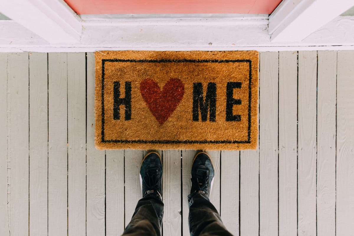 A coconut coir doormat on a covered porch with boots beside it