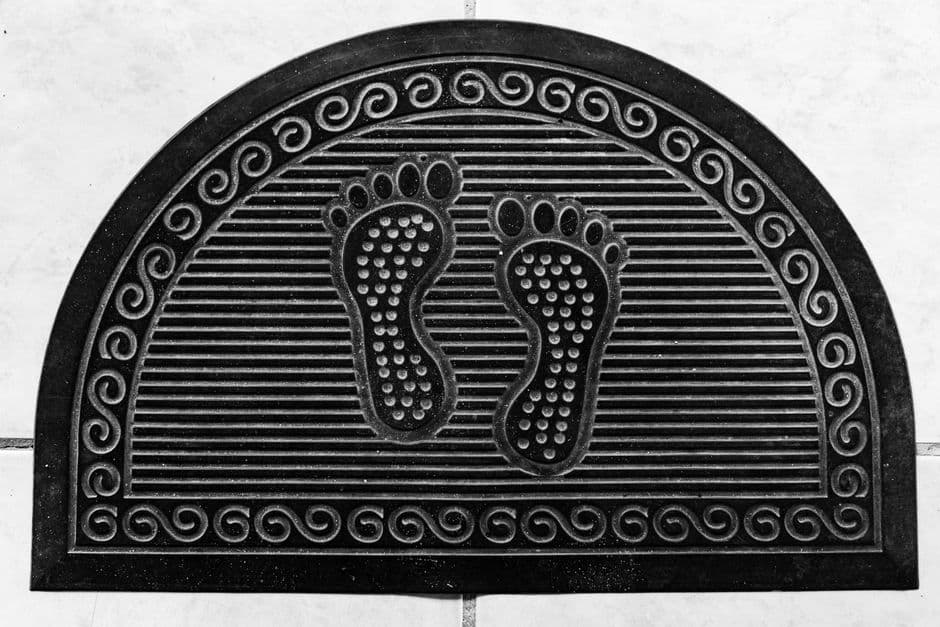 A black half-moon rubber door mat with an embossed footprint pattern
