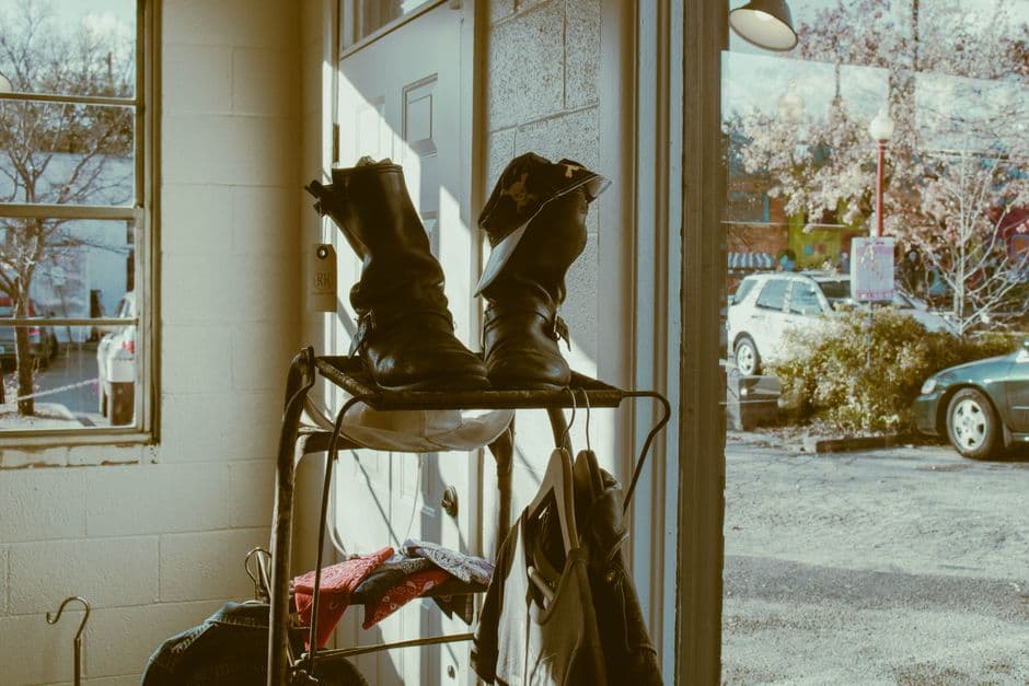 Worn brown leather boots on a wooden rack beside a sunlit doorway