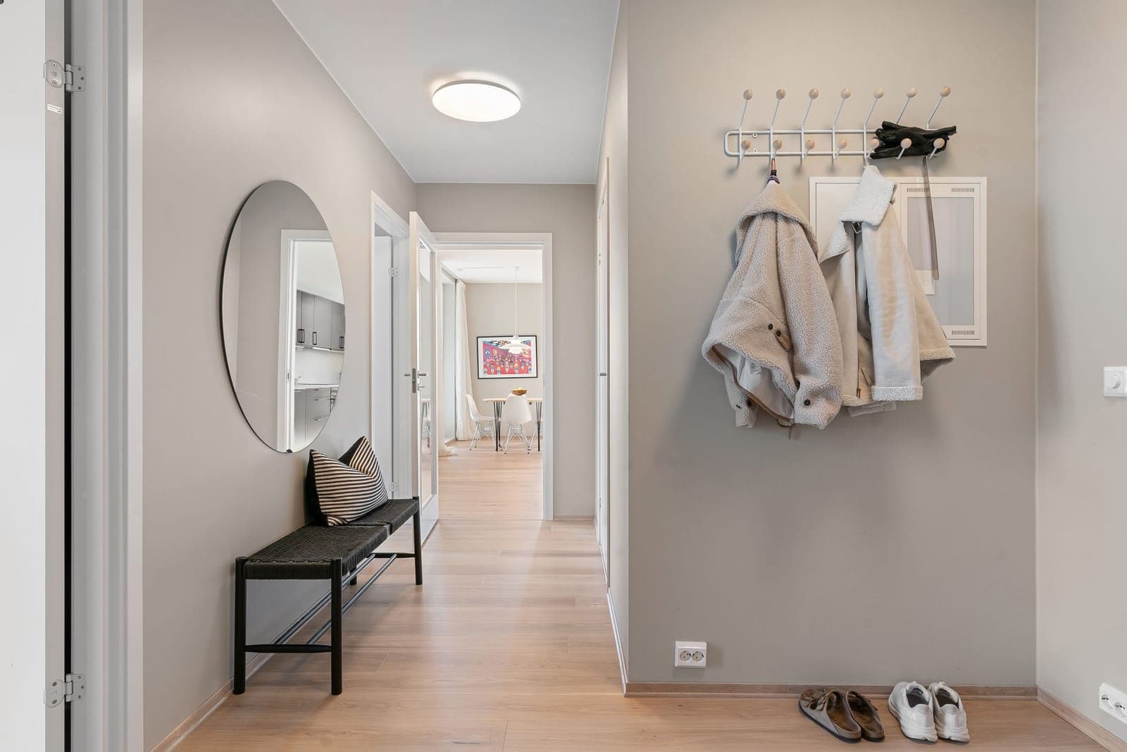 A minimalist apartment hallway with coats hanging above and shoes below