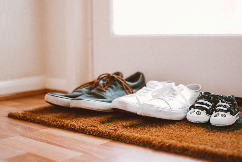 Several pairs of household shoes sitting on a doormat inside a home entrance