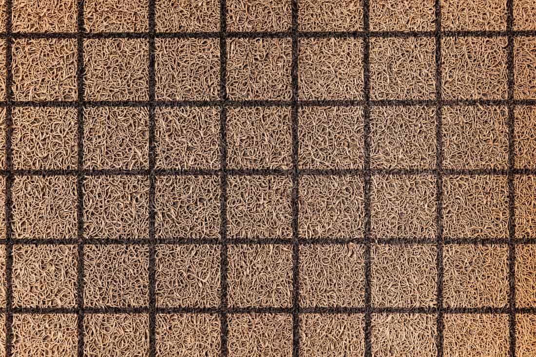 A coir doormat being shaken out and brushed on a porch
