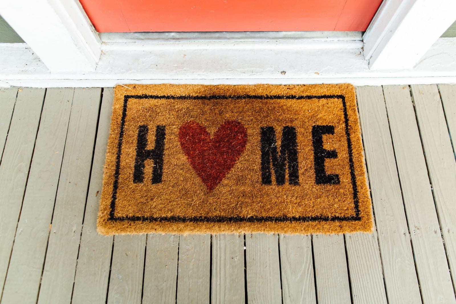 A doormat printed with the word Home on a wooden porch outside a front door
